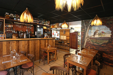 Salle intérieure du restaurant L'Oiseau à Vauvert avec tables en bois, comptoir et suspensions lumineuses.(® SAAM- fabrice CHORT)